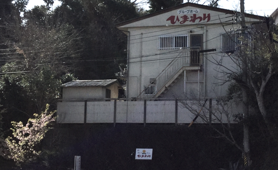 施設名が看板に見える白い2階建て建物の外観。階段と手すりが付いた玄関が特徴。