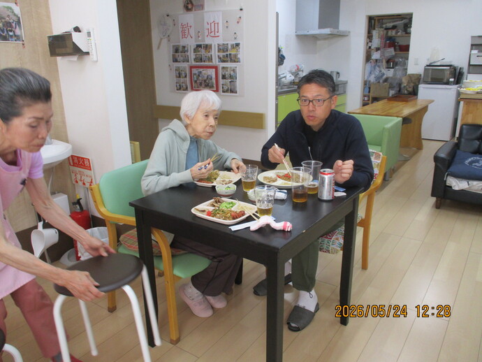 食堂で食事をする高齢者と職員。テーブルに料理と飲み物が並ぶ。