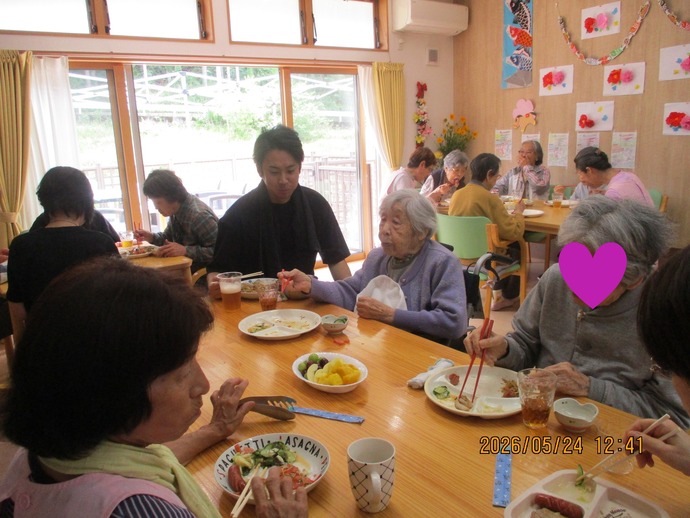 食堂で食事をする高齢者と職員。自然光の入る明るい空間で、複数の入居者が食事をしている。